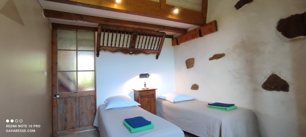 Chambre parentale du gîte L'Orangeraie avec deux lits simples 70x190, ambiance cosy et accès vers l'extérieur.