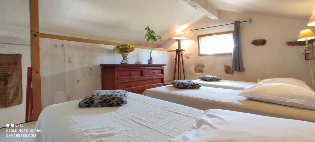 Chambre en soupente du gîte L'Orangeraie avec trois lits simples, poutres apparentes, ambiance cosy, Le Pradet.