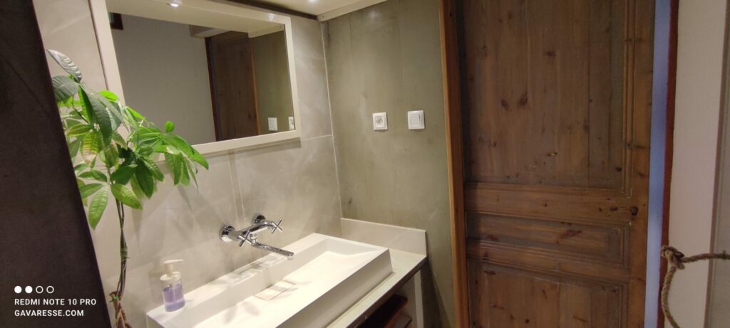 Salle de bain du gîte L'Orangeraie, béton ciré, vasque moderne, miroir, et porte en bois authentique, Le Pradet.