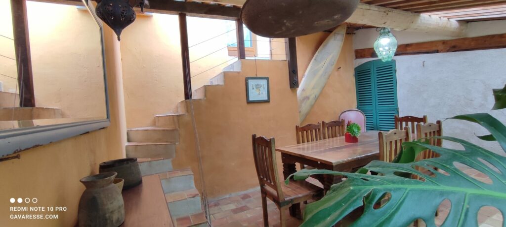 Vue de la terrasse couverte du Grand Gîte, avec escalier extérieur, table en bois et décoration locale, Le Pradet.