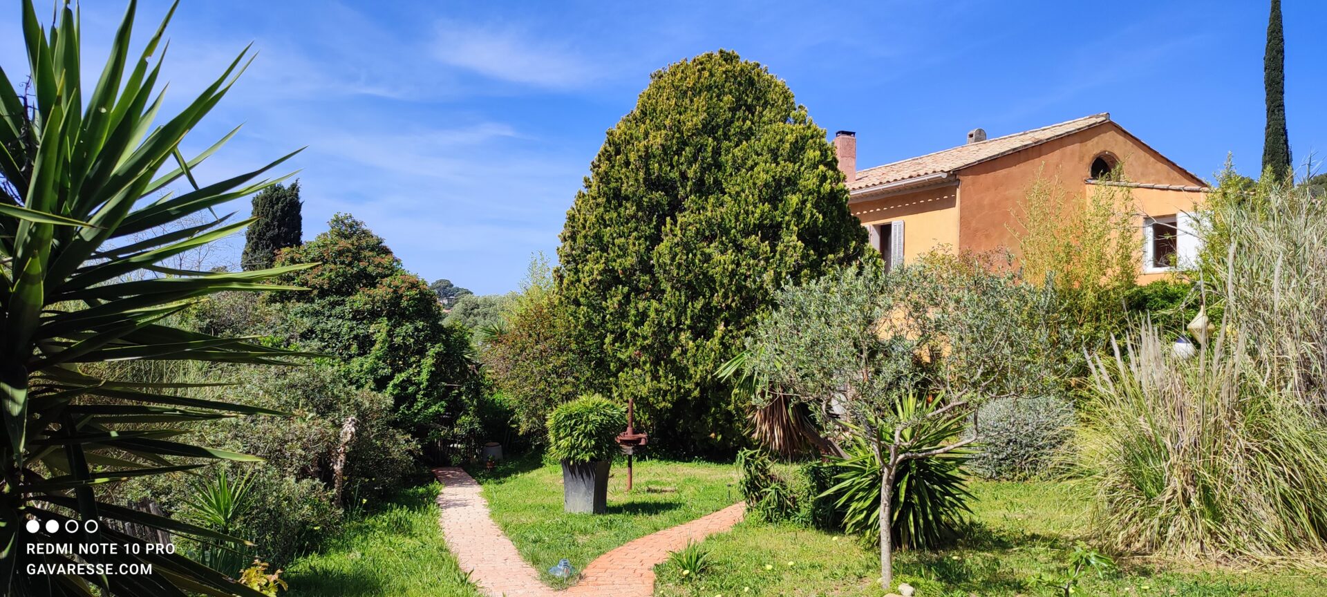 Chemin d'accès en pavés dans le jardin du Mas de la Gavaresse, avec un pressoir à raisin ancien exposé et des ganivelles en noisetier.