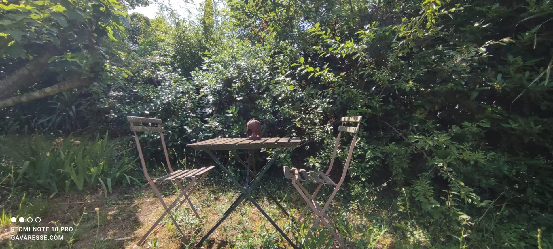 Petit coin isolé et romantique dans le jardin, avec un banc ou des chaises, entouré de verdure et de fleurs, idéal pour des moments intimes au Mas de la Gavaresse.