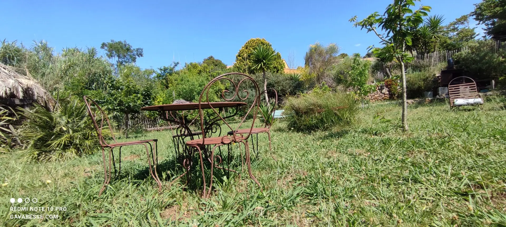 Salon de jardin en fer forgé ancien avec table, chaises et fauteuils aux motifs romantiques et volutes, sous le soleil, élégance du Mas de la Gavaresse.